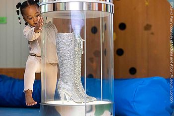 Ein kleines Mädchen schaut sich ein Paar glitzernde Stiefel an.