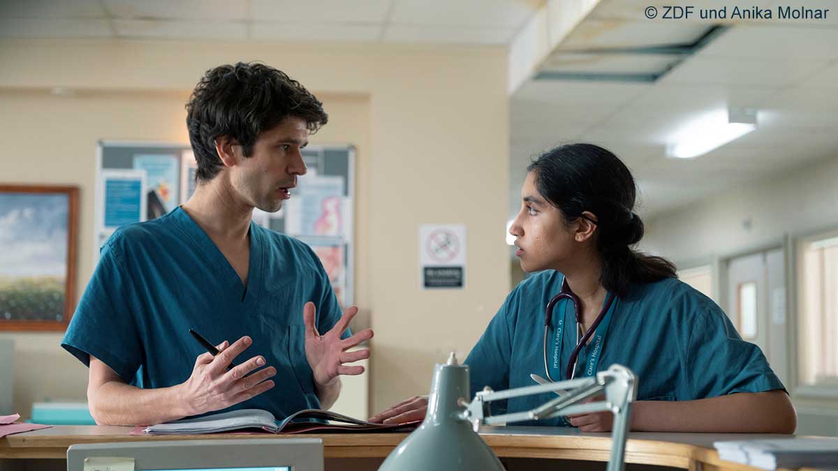 "This Is Going To Hurt - Sisyphos ist müde": Shruti (Ambika Mod) und Adam (Ben Whishaw) lehnen an der Rezeption einer Krankenstation und unterhalten sich. "This Is Going To Hurt - Sisyphos ist müde": Shruti (Ambika Mod) und Adam (Ben Whishaw) lehnen an der Rezeption einer Krankenstation und unterhalten sich.